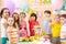 Children celebrating birthday party. Kids stand arround festive table and show thumbs up