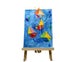 Children drawing representing sailing boats on blue paper displayed on a wooden easel.