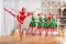 Children dressed as elves and practicing at a ballet barn look at a dancing ballerina dressed as santa claus in a spacious white