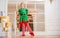 Children dressed in costumes of Christmas elves practice at a ballet bar in front of a mirror in a spacious white studio