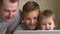 Children and father watch video on laptop, smile, have fun