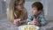 Children food, cute kid with mama eating sweets from plate lying on floor at home