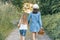 Children girls on forest road holding hands. Sunny summer day, girl holding basket with berries