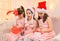 Children girls portrait, sisters dressed in santa helper hat, sitting on a couch in home interior decorated with christmas lights