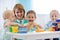 Children group playing with teacher in day care centre. Carer and babies at table in nursery playroom