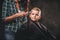 Children hairdresser with the trimmer is cutting little boy against the dark background. Cute preschooler boy getting