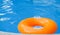 Children inflatable orange swimming ring with white handles floating in blue pool. Top view, close-up. Copy space for text