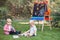 Children kids, boy and girl sitting in grass outside by drawing easel with books reading studying learning