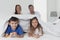 Children lying under blanket while parent sitting on bed in bedroom at home