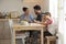 Children Paint At Kitchen Table As Parents Look At Laptop