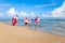 Children with parent wearing colorful inflatable swim ring running on summer beach, kids and adult on tropical sand beach, happy