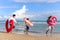 Children with parent wearing colorful inflatable swim ring running on summer beach, kids and adult on tropical sand beach, happy