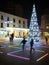 Children playing around a Christmas tree in a street with people walking and a floor with brightly coloured lines