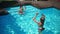 Children playing with ball in swimming pool in slow motion. High angle view of happy hyperactive Caucasian boy and girl