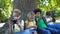 Children playing gadgets, sitting under tree in park, boy smiling in camera, app