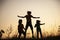 Children playing jumping on summer sunset meadow silhouetted