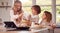 Children In Pyjamas Making Pancakes In Kitchen At Home Following Recipe On Digital Tablet