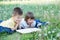 Children reading book in park lying on stomach outdoor among dandelion in park, cute children education and development