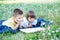 Children reading book in park lying on stomach outdoor among dandelion in park, cute children education and development