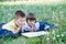 Children reading book in park lying on stomach outdoor among dandelion in park, cute children education and development