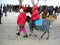 Children in red jackets have fun in the winter on holiday. One girl leads a small horse, the second girl sits on the back of a