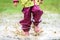 Children in rubber boots and rain clothes jumping in puddle.