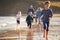 Children Run Ahead As  Multi-Generation Family Walk Along Shore On Winter Beach Vacation