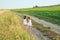 Children run hand in hand in the fresh air among fields and meadows on a narrow sandy path.