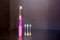 Children`s electric pink toothbrush with backlight with three interchangeable nozzles stands on a dark shelf
