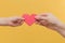 Children`s hand and the hand of a woman hold a red heart by the edges on a yellow background. The idea is peace, mutual