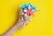 Children`s hand holds a bouquet of paper flowers made using the origami technique on a yellow background. DIY concept. Children`s