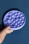Children& x27;s hand is playing with a purple popit toy on a blue background. Anti-stress silicone sensory toy. Trend of 2021