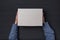 Children`s hands holds white cardboard box on black background. Top view. Shipping concept