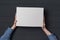 Children`s hands holds white cardboard box on black background. Top view. Shipping concept