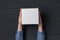 Children`s hands holds white square cardboard box. Black background. Top view. Shipping concept
