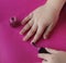 Children`s hands paint their nails with pink shiny nail polish.