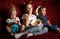 Children`s movies: Three children watch movies at home on a big red sofa in the dark and eat popcorn.