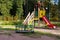 Children`s playground in the park against the background of autumn trees on a bright fine day. Multi-colored slide and carousel