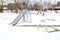 Children`s playground in winter under snow. Swing, carousel and slide. Winter desolation