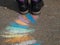 Children`s Rainbow chalk drawing art on asphalt painted with colored crayons and girl`s feet in boots on colorful road