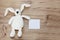 Children`s toy soft white plush rabbit with long ears holds a greeting card on a wooden background