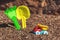 Children`s toy truck with gravel or sand. Yellow scoop and green rake on the background. Concept of transportation of