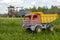 A children`s toy truck is standing in the grass against the background of real working trucks.  Concept: harvesting, help from th