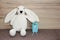 Children`s toy white plush rabbit holding a blue gift box on a brown background