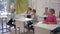 Children at school, boys and girls sit at desks and raise hands during lesson in classroom in school