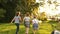 Children schoolchildren running into the distance on the background of green trees and sunset. The boy makes a flip on