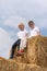 Children sit on a haystack on sunny day. Two friends are sitting on the hay and look at the camera against the blue sky. Vertical