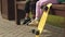 Children are sitting on a bench, moving their legs, a yellow skateboard is standing next to it.