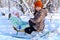 Children sitting on sledge in the winter forest and playing, bright sunlight and shadows on the snow, beautiful nature