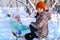 Children sitting on sledge in the winter forest and playing, bright sunlight and shadows on the snow, beautiful nature